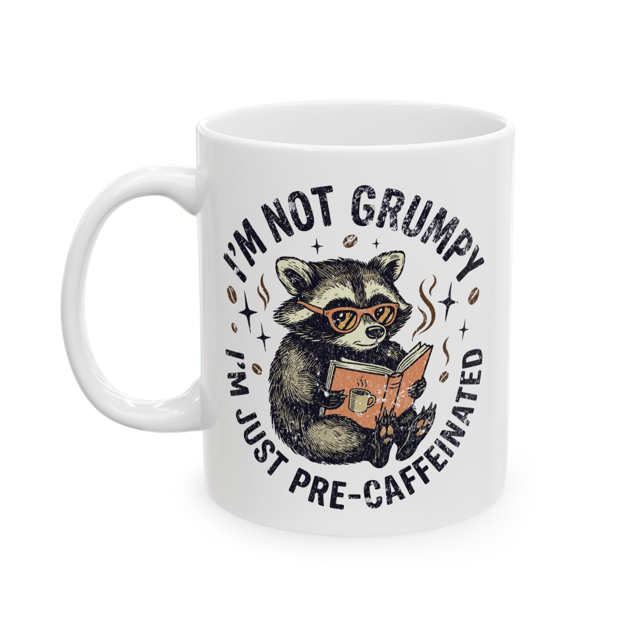 White ceramic mug featuring a raccoon wearing glasses and reading a book with coffee-themed text.