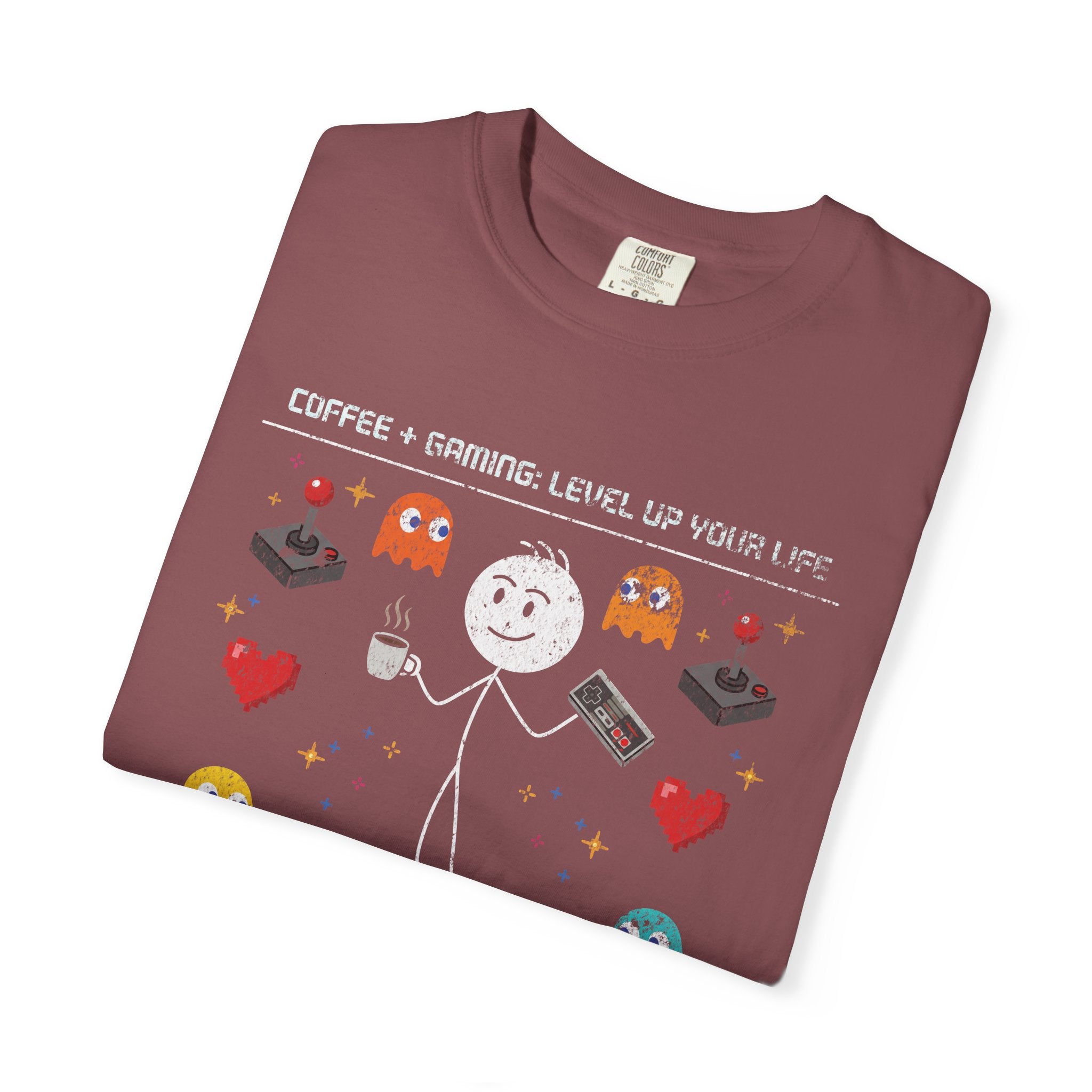 A folded maroon t-shirt featuring a stick figure graphic with coffee and retro gaming elements.