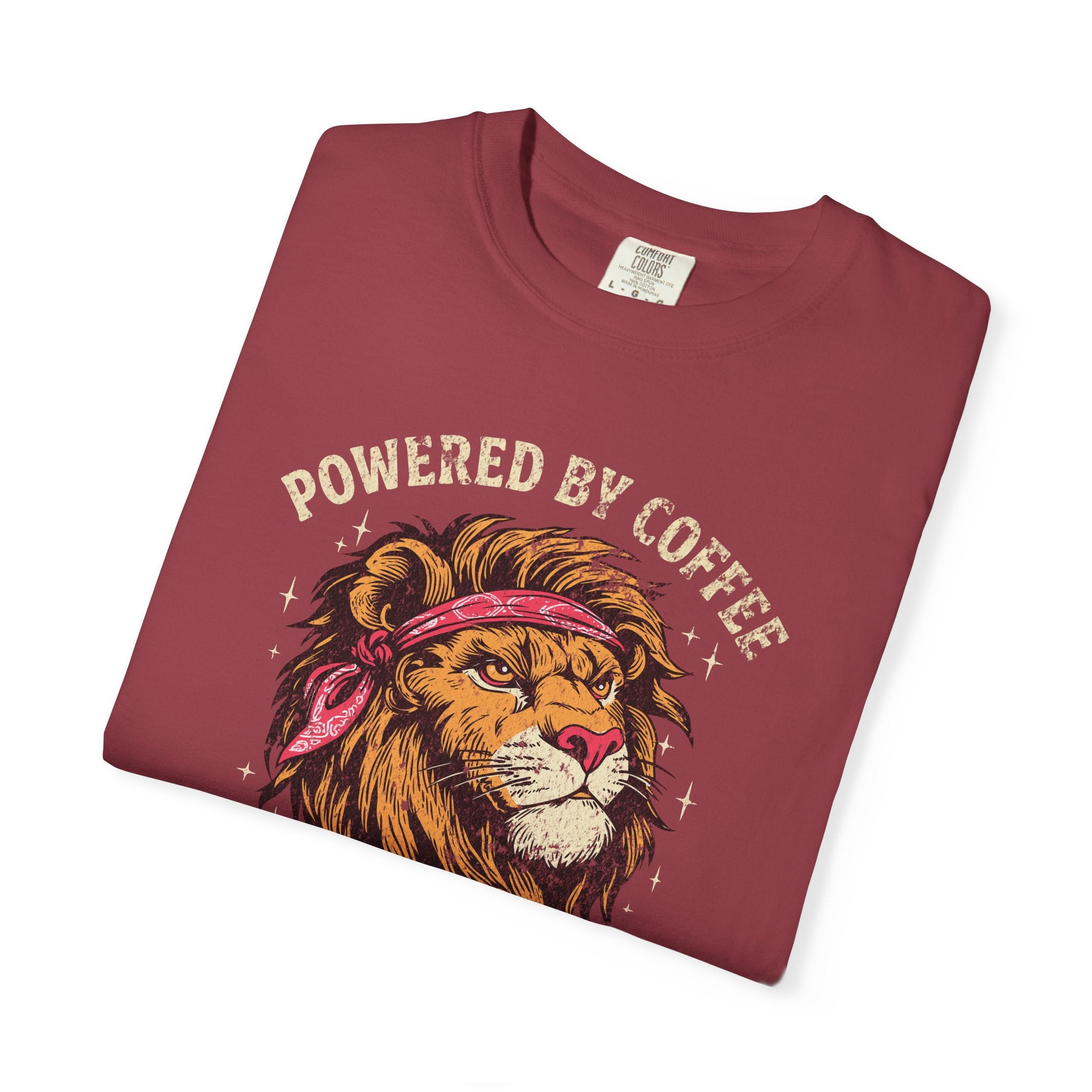 A folded maroon t-shirt featuring a graphic of a lion wearing a bandana with Powered by Coffee text.