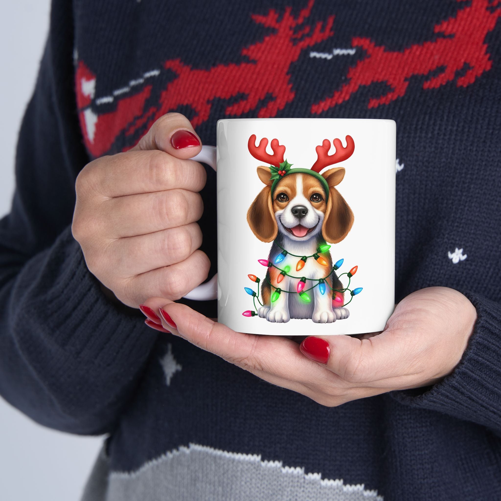 A person holds a white ceramic mug featuring a beagle wearing reindeer antlers and Christmas lights.