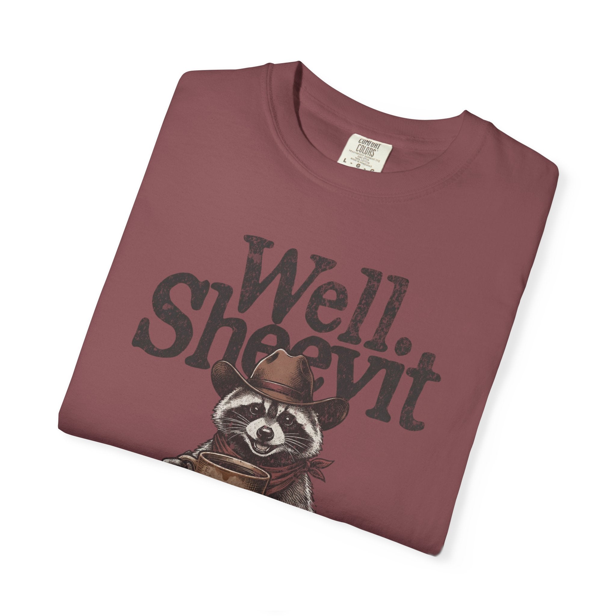 A maroon t-shirt featuring a graphic of a raccoon in a cowboy hat holding a coffee mug.