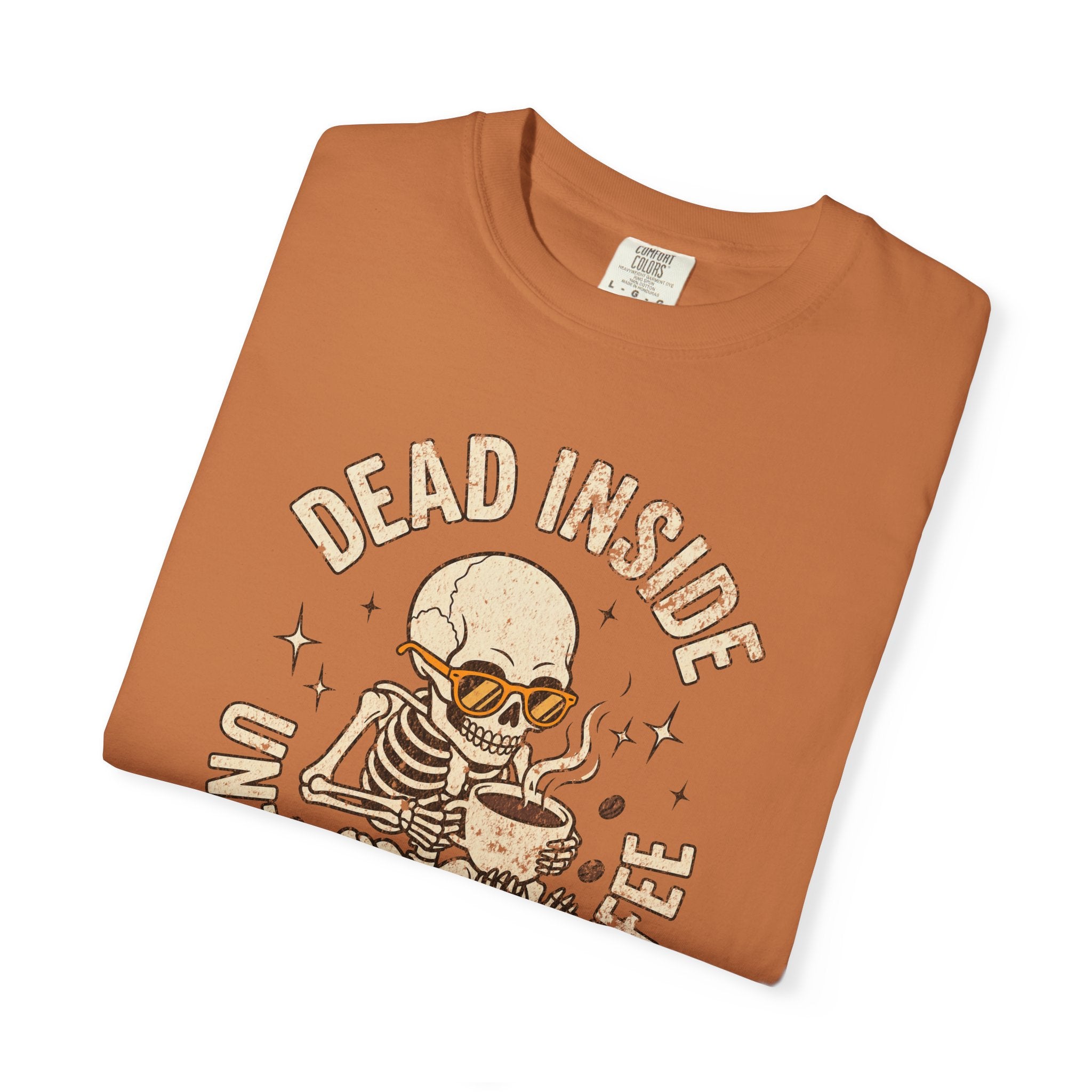 Folded orange t-shirt with a distressed graphic of a skeleton wearing sunglasses drinking coffee.