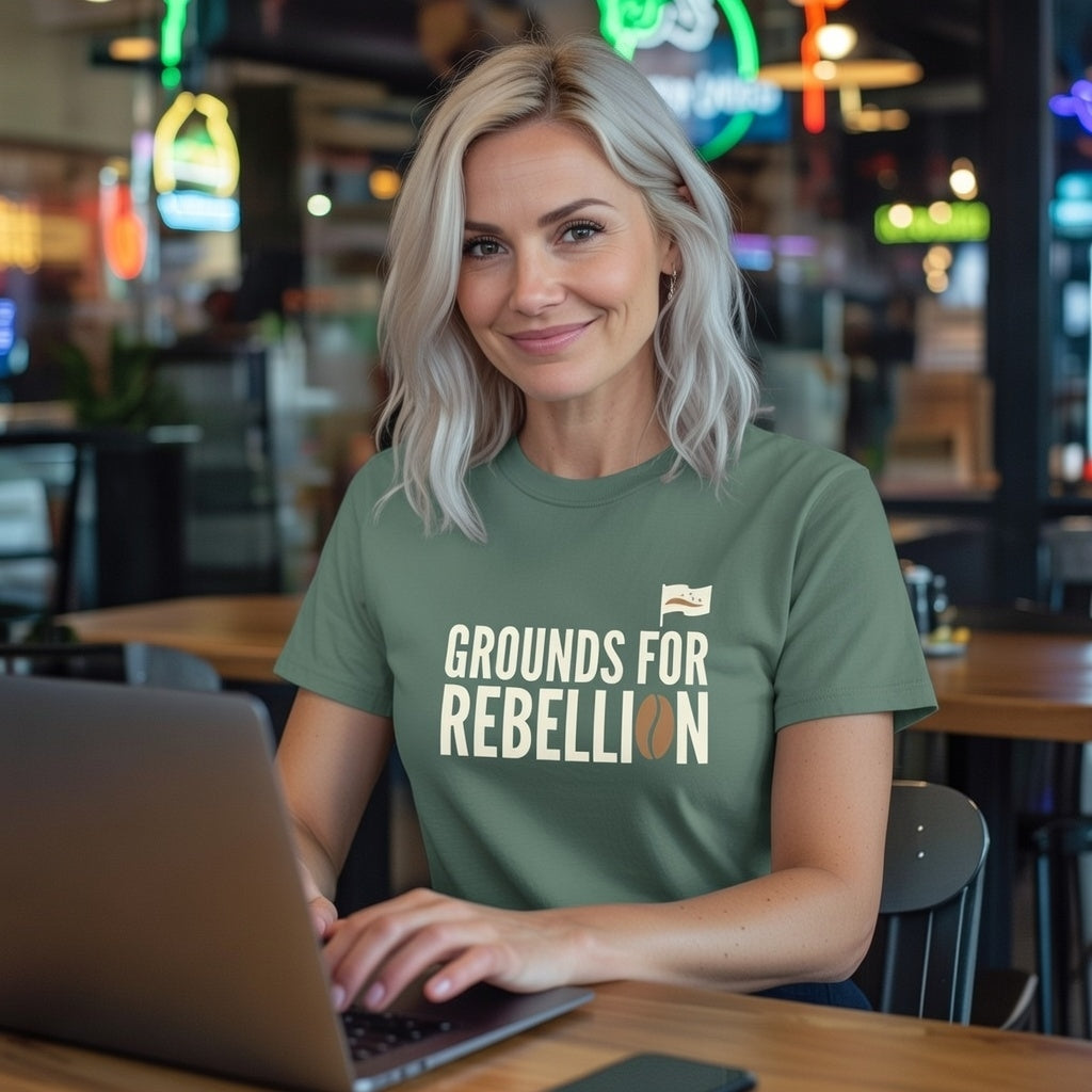 A woman wears a sage green t-shirt with the text Grounds For Rebellion and a coffee bean graphic.