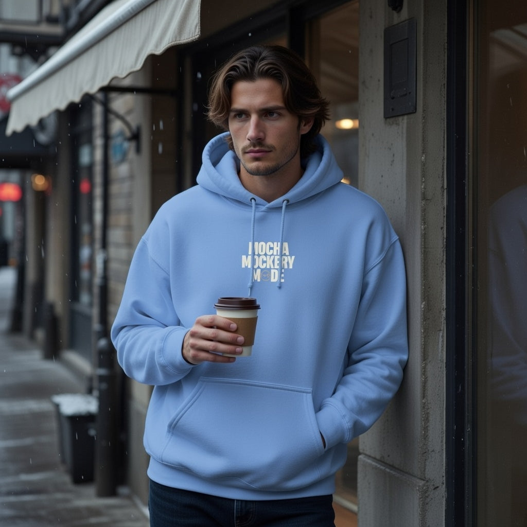 A man wears a light blue Mocha Mockery Mode hoodie while holding a coffee cup on a city street.