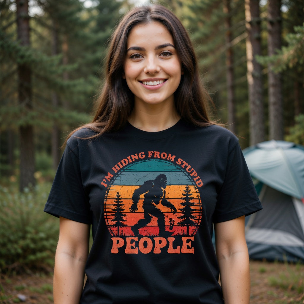 A woman wears a black t-shirt featuring a distressed Bigfoot graphic and the text I'm Hiding From Stupid People.