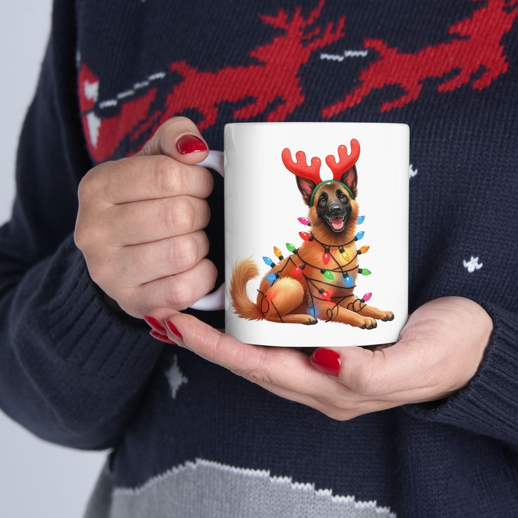 A person in a festive sweater holds a white mug with a Belgian Malinois wearing antlers and lights.