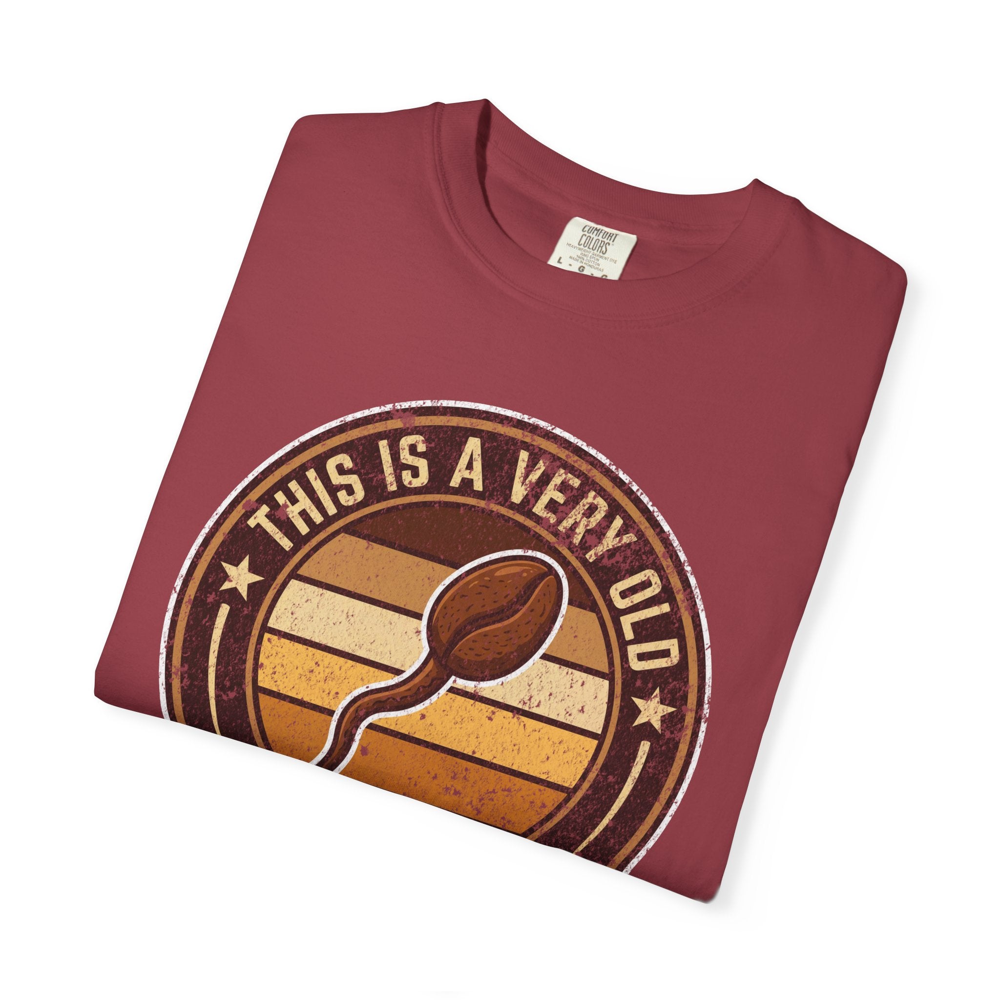 A folded maroon t-shirt with a distressed vintage graphic of a coffee bean and text.