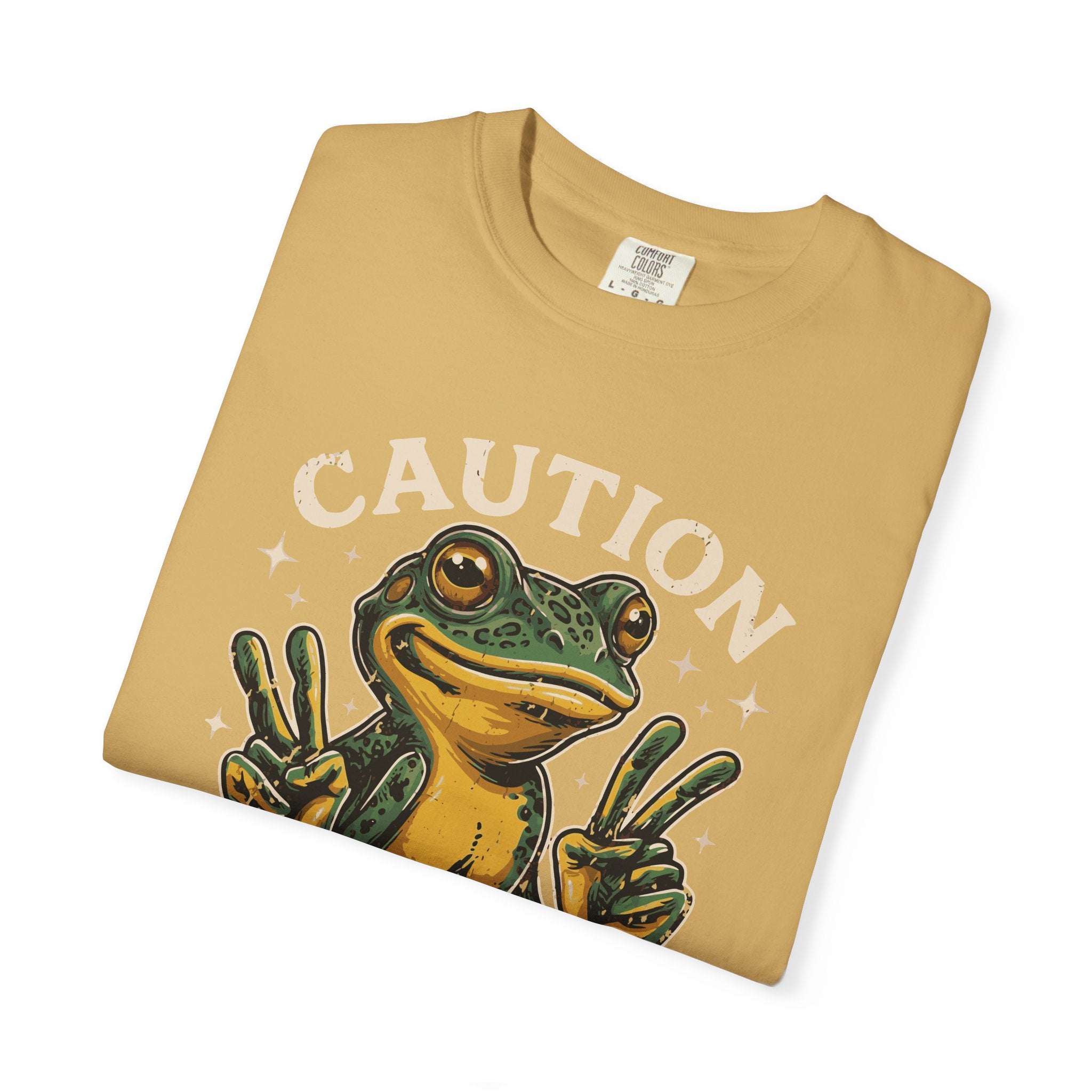 Folded mustard yellow t-shirt featuring a graphic of a frog making peace signs with the word CAUTION