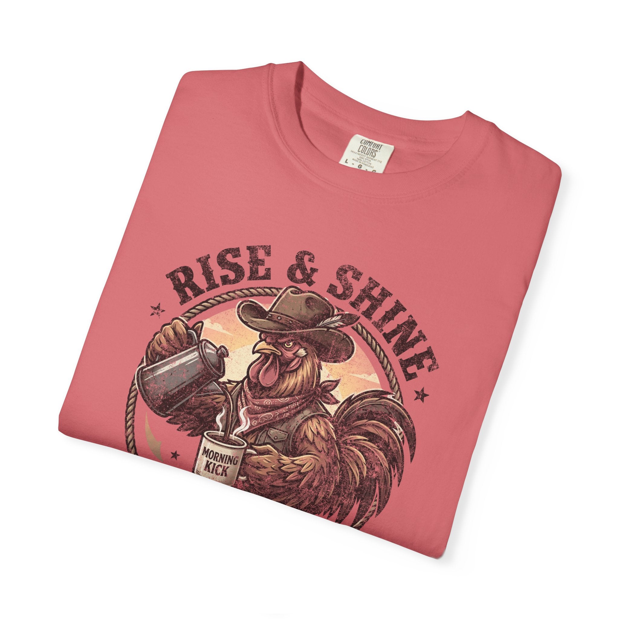 A folded coral-colored t-shirt featuring a graphic of a cowboy rooster pouring coffee.