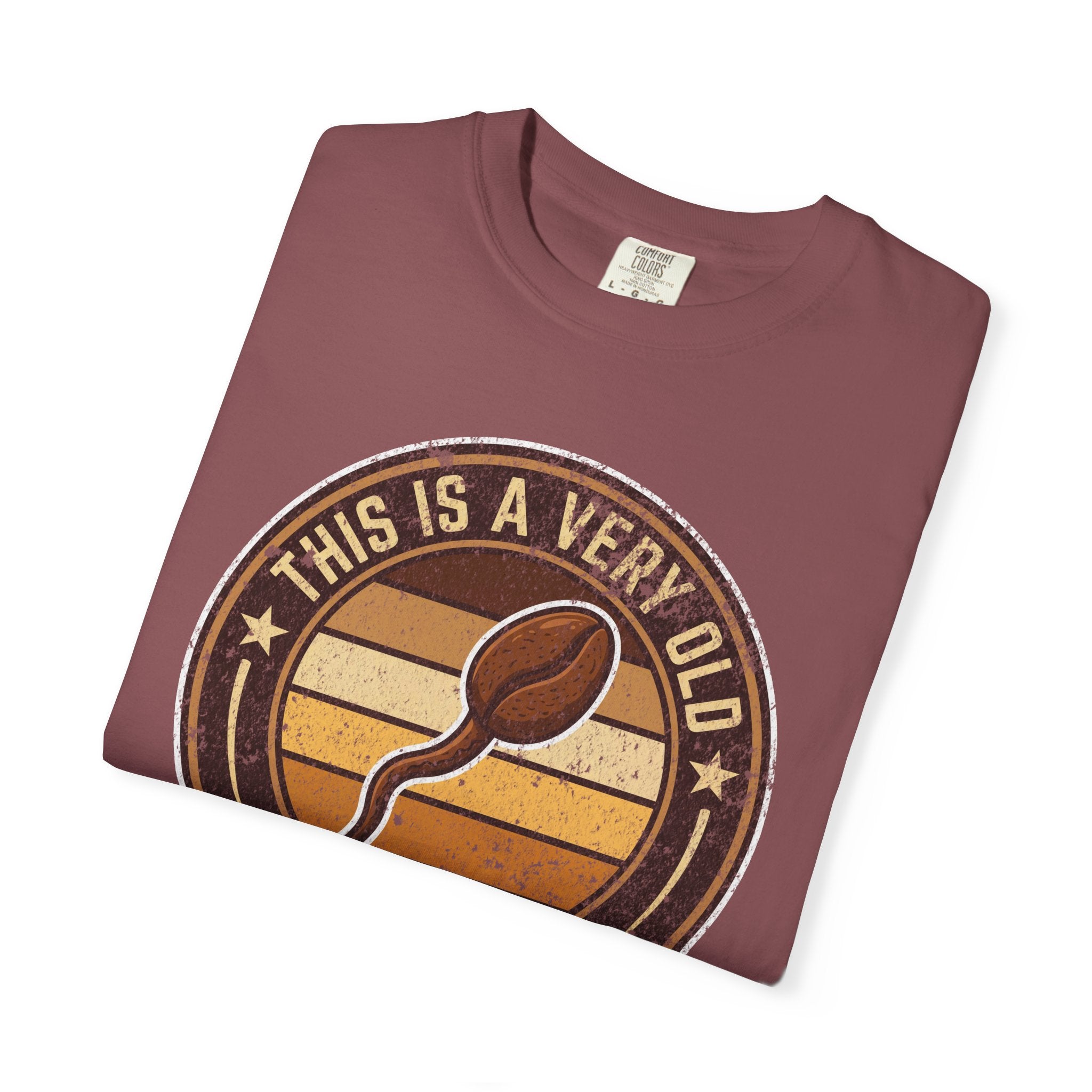 A folded maroon t-shirt featuring a vintage-style graphic of a coffee bean and text.