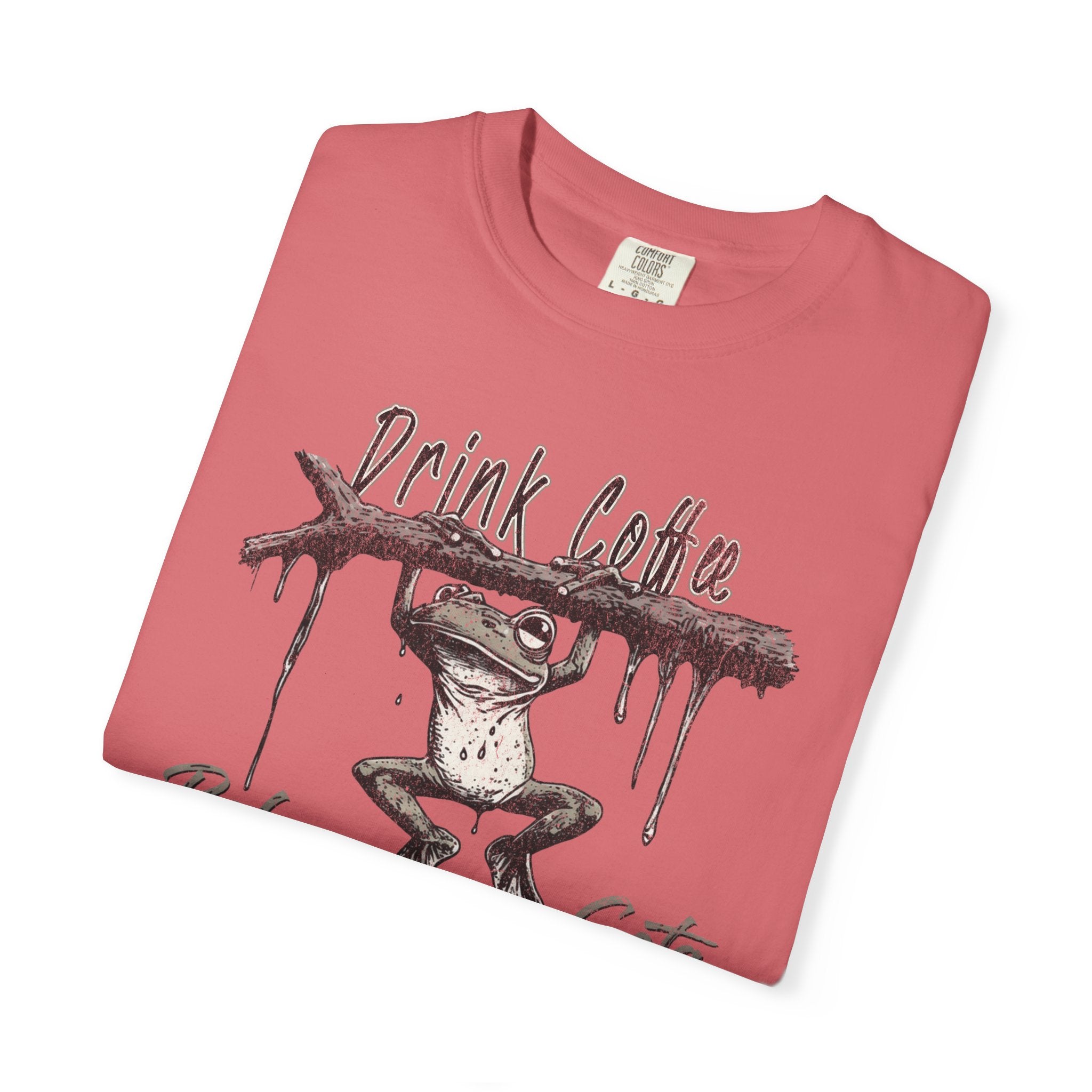 A folded coral-colored unisex t-shirt featuring a graphic of a frog hanging from a branch.