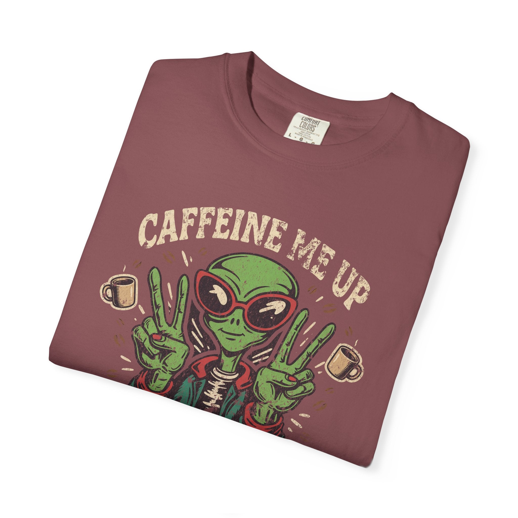 A folded maroon unisex cotton t-shirt featuring a distressed graphic of an alien making peace signs.