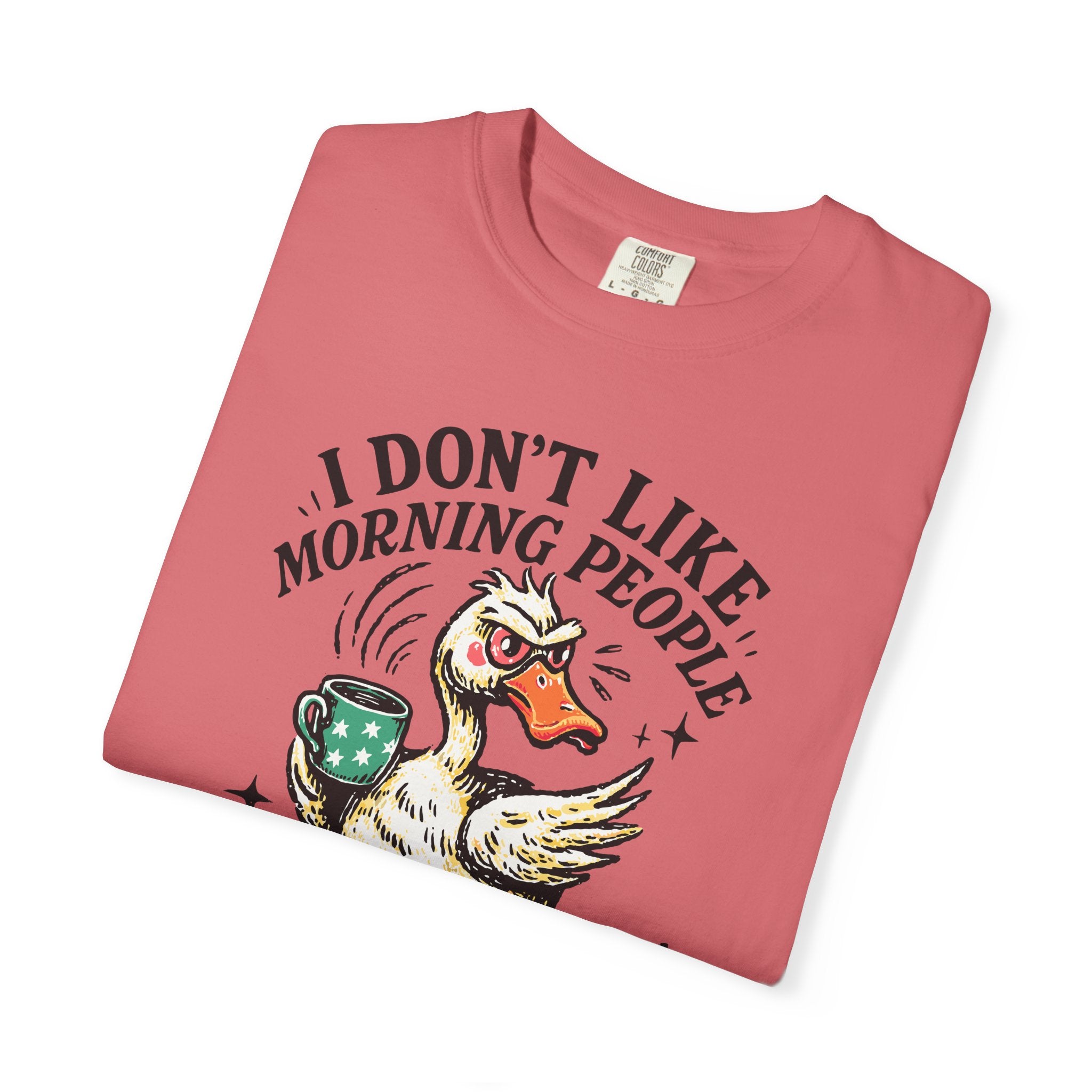 A folded coral-colored t-shirt featuring a graphic of a grumpy duck holding a coffee mug.