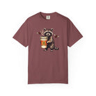 A maroon Comfort Colors 1717 unisex t-shirt featuring a graphic of a raccoon holding a coffee cup.