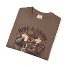Brown graphic t-shirt featuring a cowboy rooster pouring coffee with the text Rise & Shine.