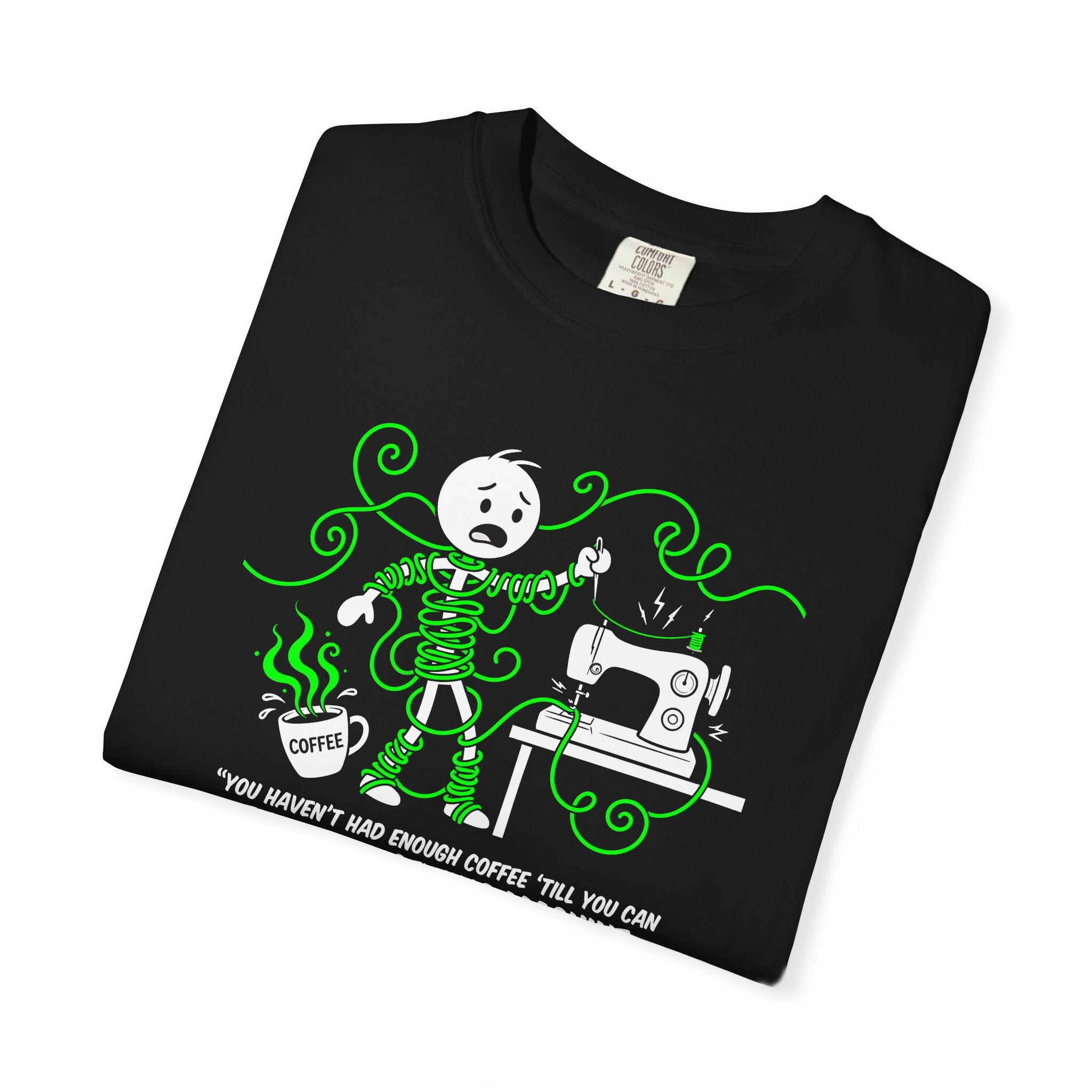 Black t-shirt featuring a stick figure tangled in green thread while sewing, with coffee nearby.