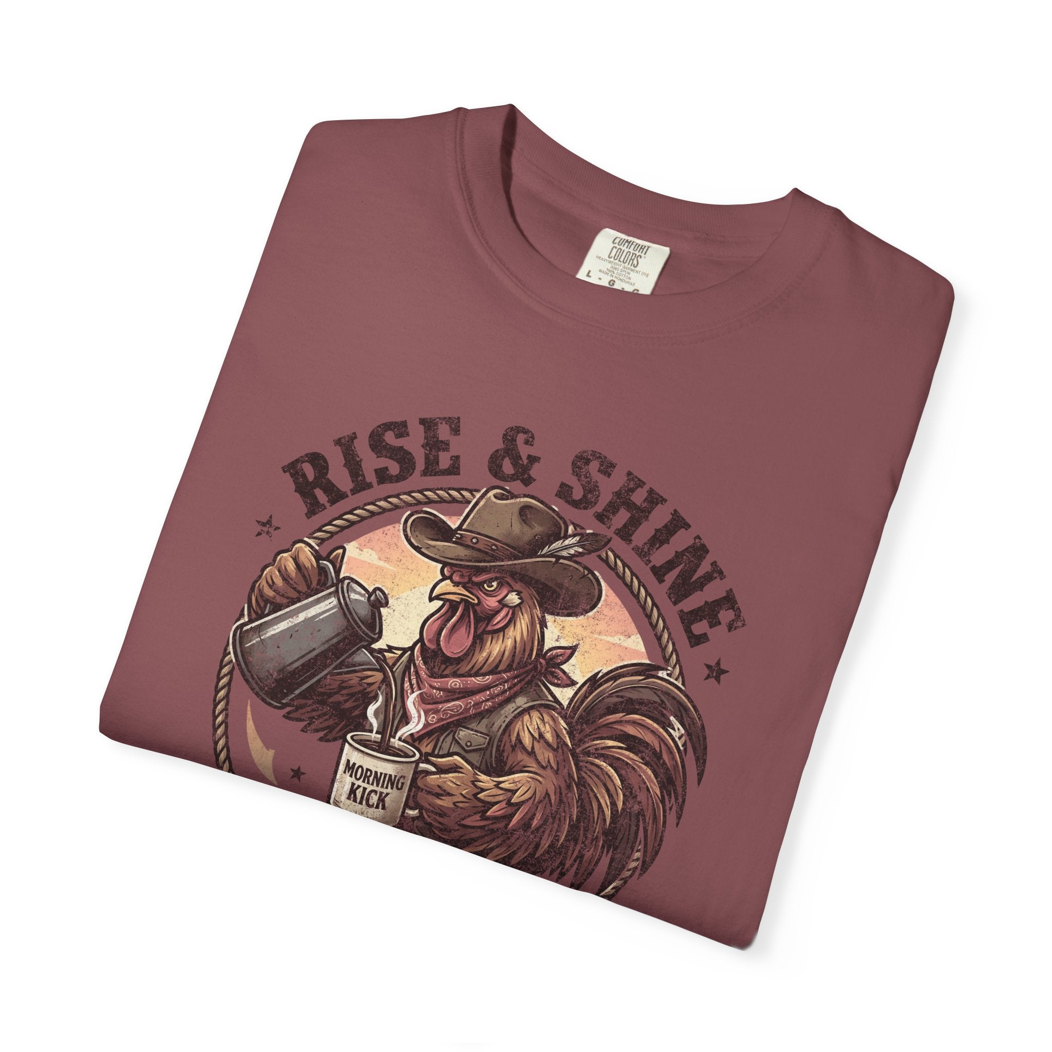Folded maroon graphic t-shirt featuring a cowboy rooster pouring coffee with Rise & Shine text.
