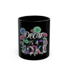 Black ceramic coffee mug with floral design and the text Decaf Is A Joke.