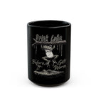 Black ceramic mug featuring a frog hanging from a branch above a crocodile with coffee text.
