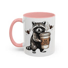 White ceramic mug with a pink handle and interior, featuring a raccoon holding a coffee cup.