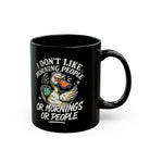 Black ceramic coffee mug featuring a grumpy duck illustration and text about disliking mornings.
