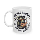 White ceramic mug featuring a raccoon wearing glasses and reading a book with coffee-themed text.