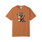 Rust-colored Comfort Colors unisex t-shirt featuring a raccoon holding a coffee cup with a skull.