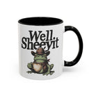 White ceramic mug with a black handle featuring a cowboy frog holding a coffee cup.