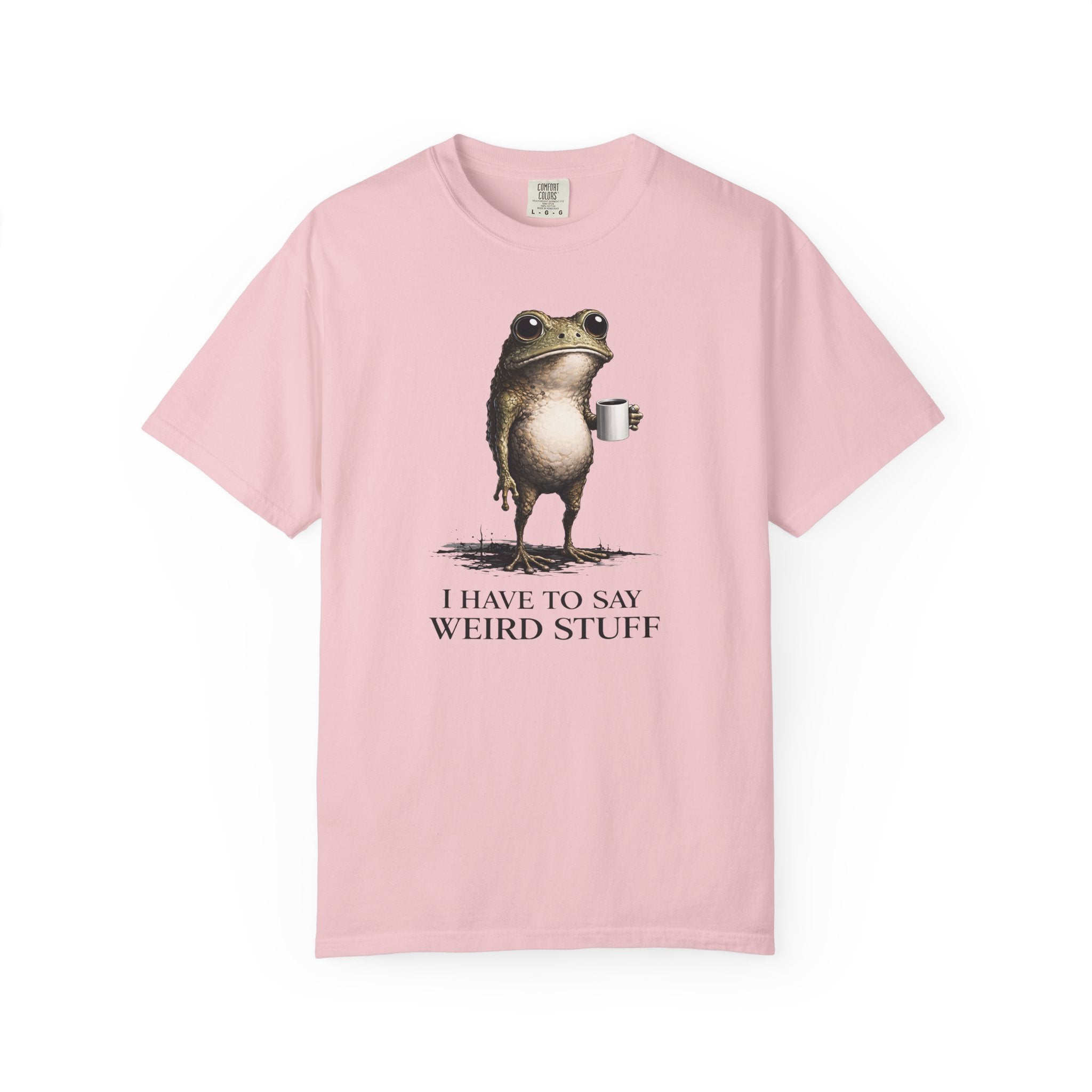 A light pink cotton t-shirt featuring a graphic of a frog holding a coffee mug with the text I HAVE TO SAY WEIRD STUFF.