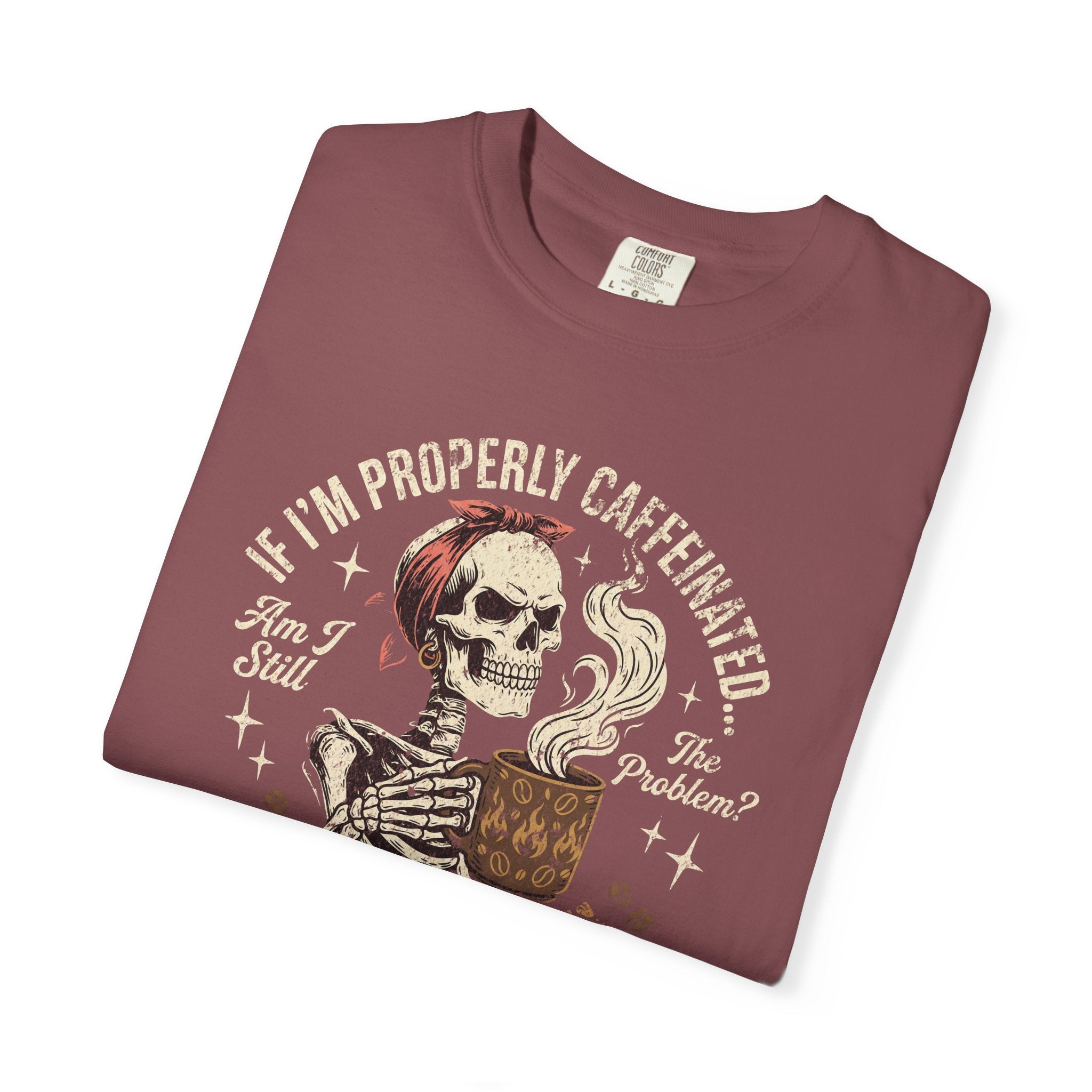 A folded maroon t-shirt featuring a graphic of a skeleton holding a steaming coffee mug.
