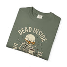 Olive green t-shirt with a distressed graphic of a skeleton wearing sunglasses drinking coffee.