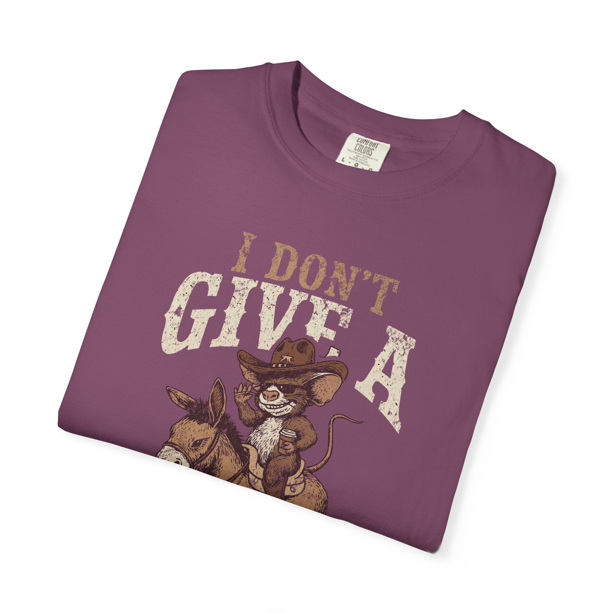 A folded purple cotton t-shirt featuring a graphic of a rat in a cowboy hat riding a donkey.