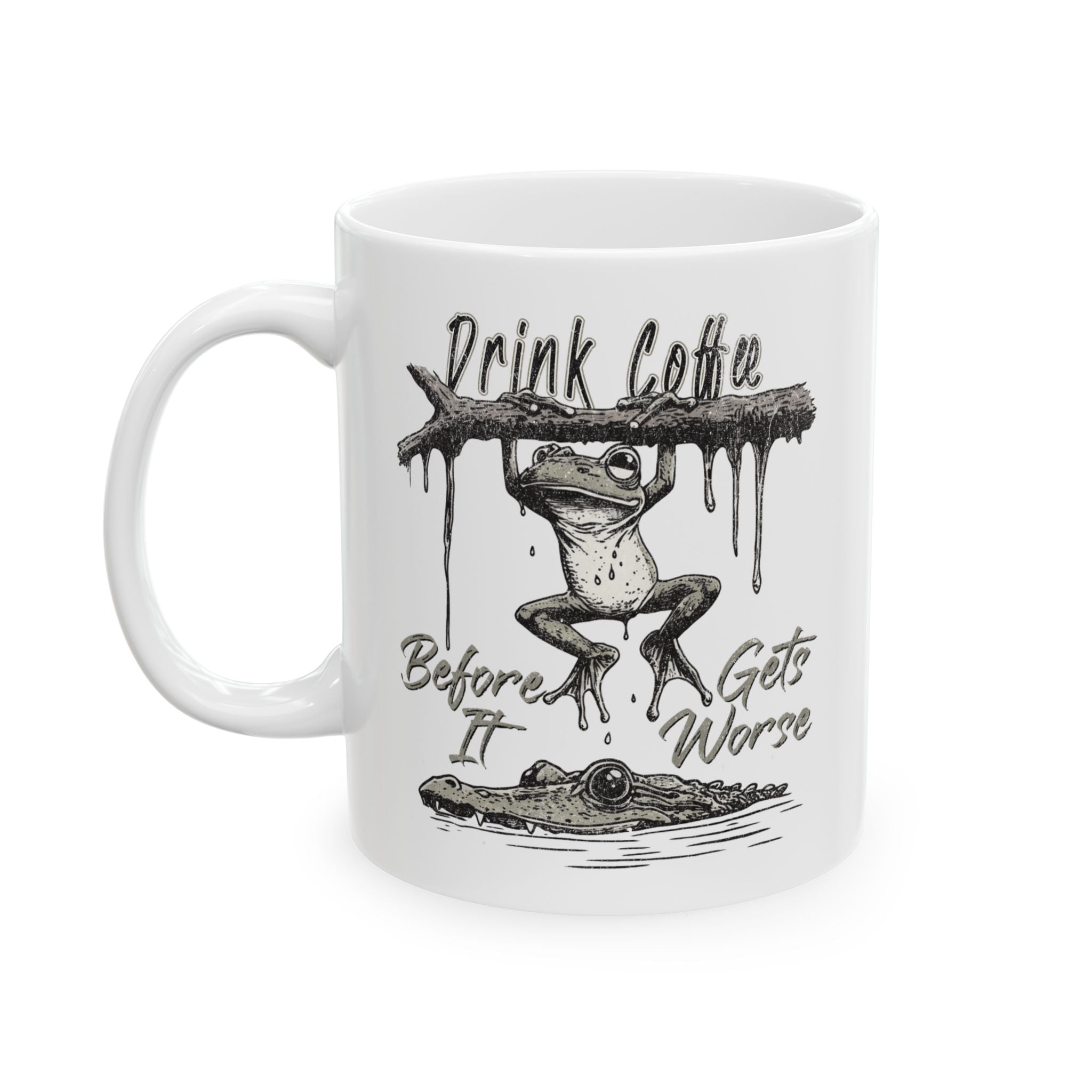 White ceramic coffee mug featuring a frog hanging from a branch above a crocodile.
