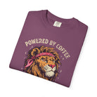 A folded purple t-shirt featuring a graphic of a lion wearing a bandana with Powered by Coffee text.