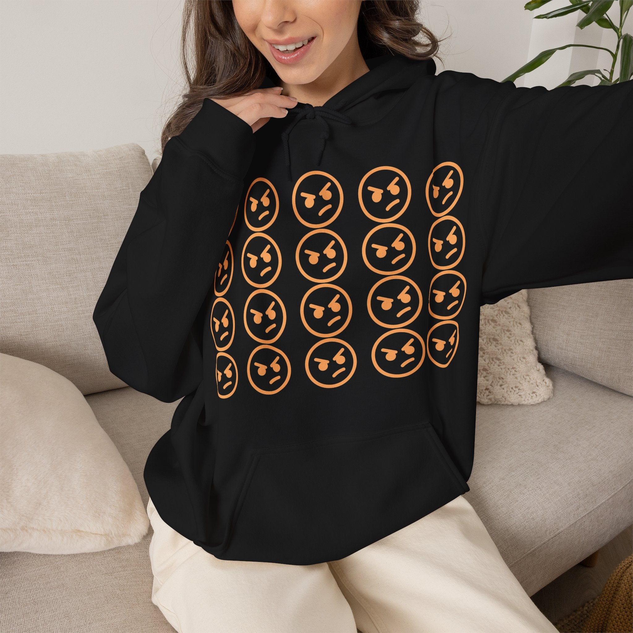 Woman wearing a black Mocha Mockery hoodie with a grid of orange angry face emojis on the front.