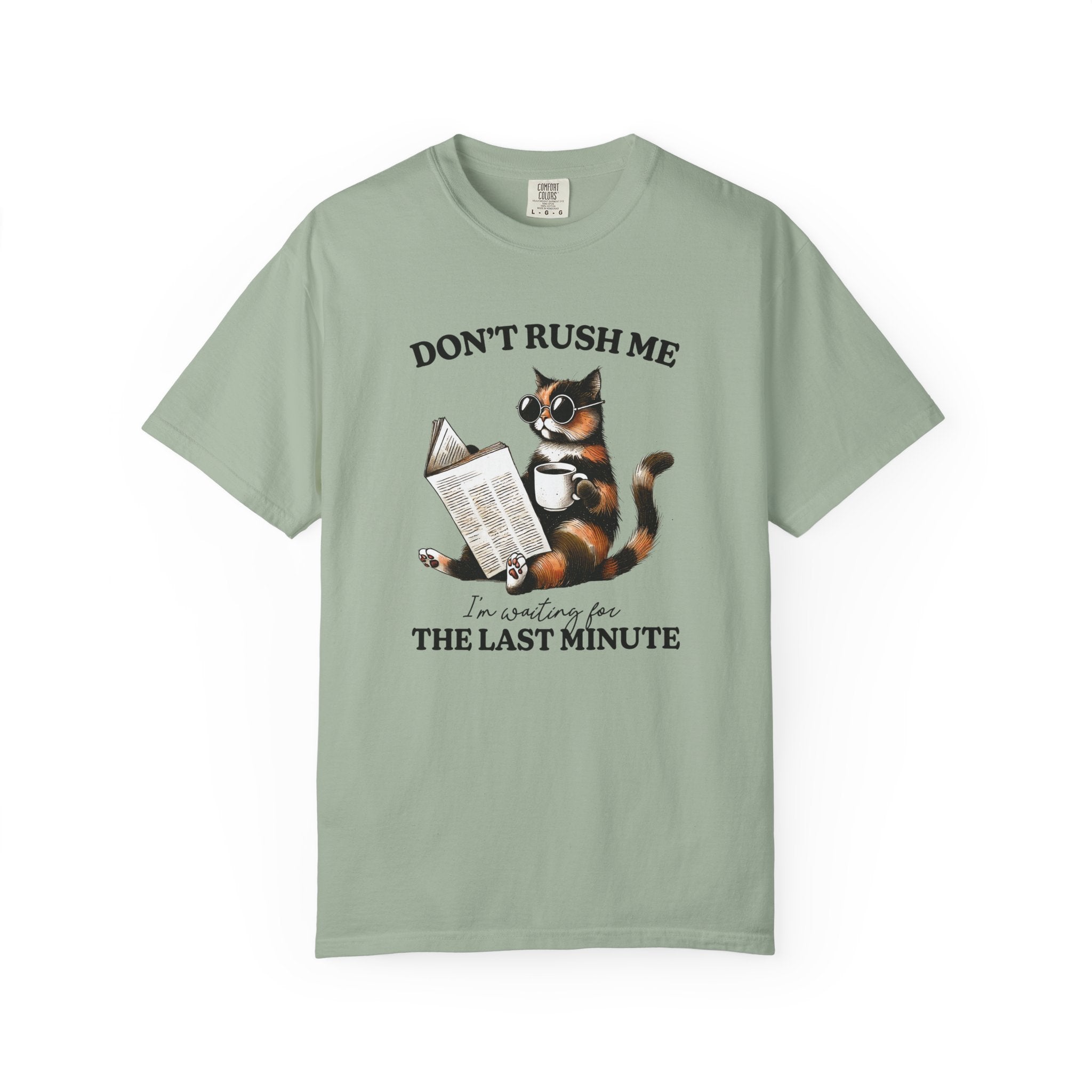 A sage green cotton t-shirt featuring a graphic of a cat wearing sunglasses reading a book.