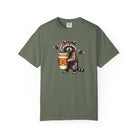 Olive green Comfort Colors 1717 unisex t-shirt featuring a raccoon holding a coffee cup.