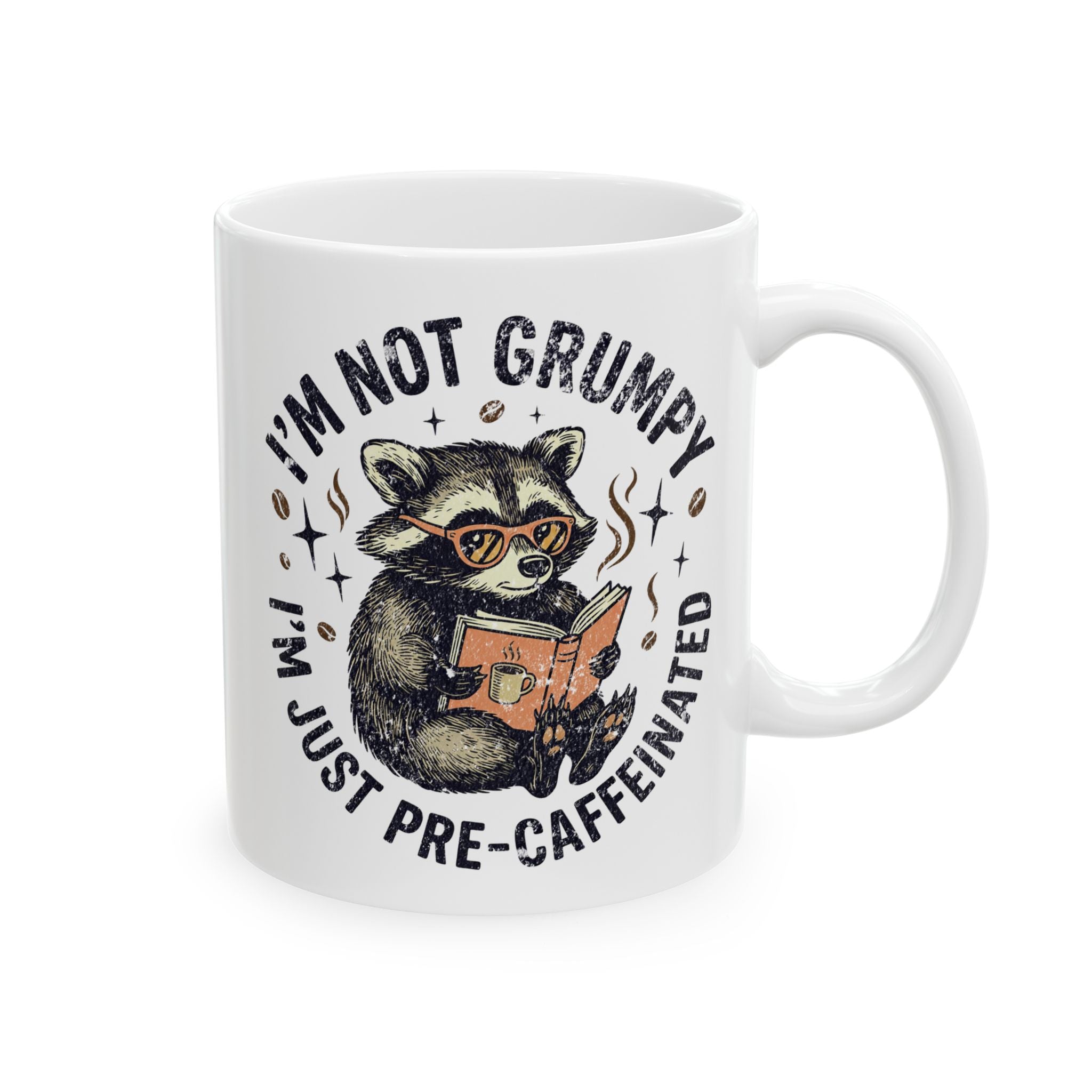 White ceramic coffee mug featuring a raccoon wearing glasses and reading a book.