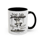 White ceramic mug with a black handle and rim, featuring a frog hanging over a crocodile.