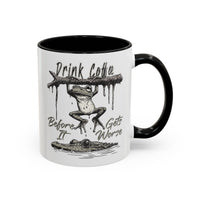 White ceramic mug with a black handle and rim, featuring a frog hanging over a crocodile.