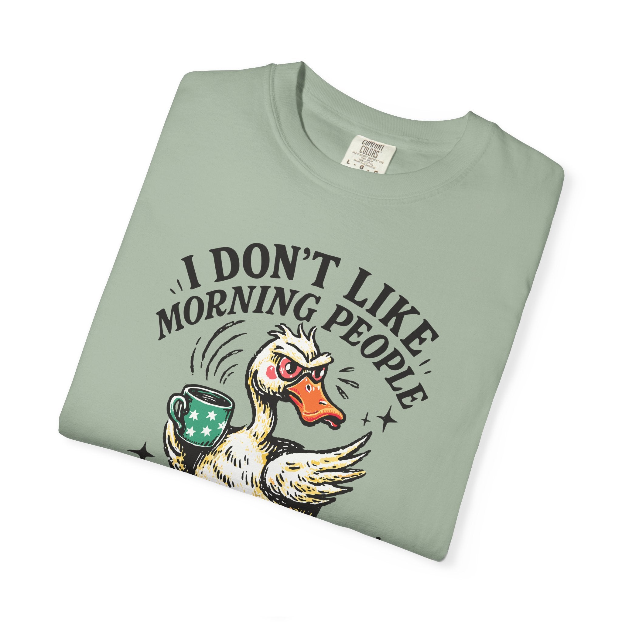 Sage green t-shirt featuring a grumpy duck holding a coffee mug with the text I Don't Like Morning