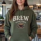 A woman wears an olive green hoodie with "BREW GOOD VIBES" and a coffee cup graphic.