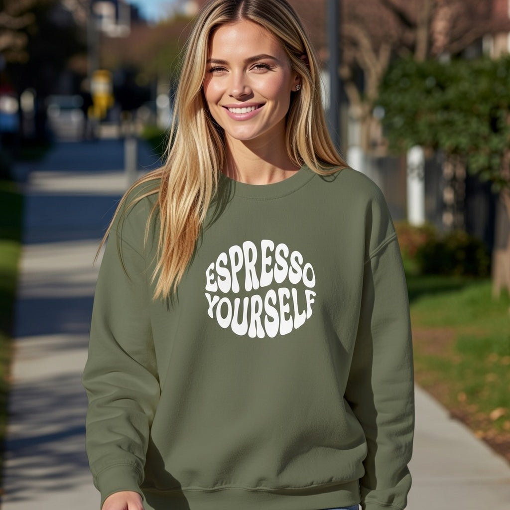 A woman smiles in an olive green crewneck sweatshirt featuring a white Espresso Yourself graphic.