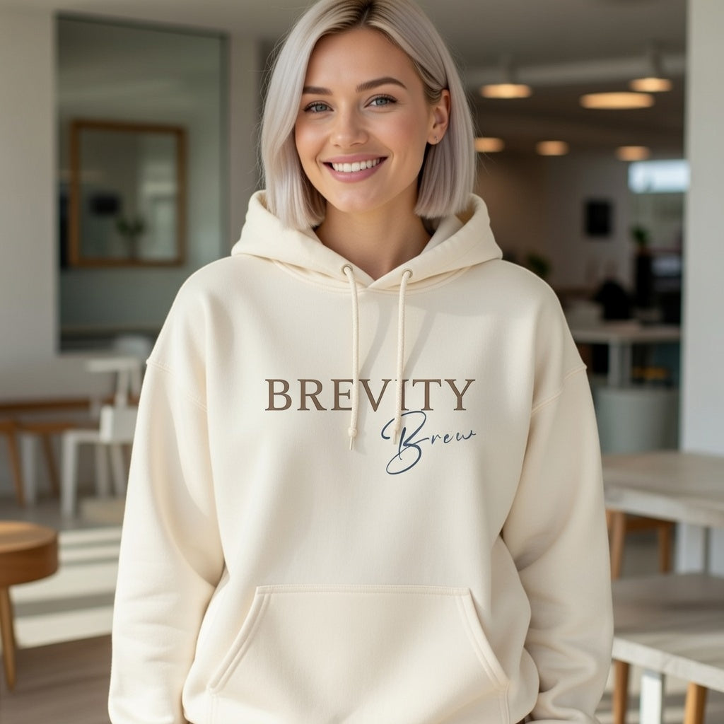 Minimalist cream-colored Brevity Brew hoodie with a script logo worn by a smiling woman.