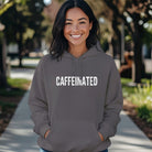 A woman smiles wearing a charcoal grey hoodie with the word CAFFEINATED printed in white.