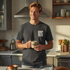 A man in a kitchen wearing a charcoal t-shirt with the text Drip With Sarcasm on the chest.