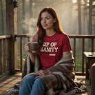 A woman on a porch wears a red Sip Of Sanity t-shirt while holding a steaming mug of coffee.