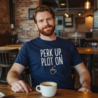 A person wearing a Perk Up, Plot On t-shirt with a minimalist coffee-themed graphic for writers.