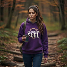 A woman in a forest wearing a purple Filterless Fuel sweatshirt and holding a coffee mug.