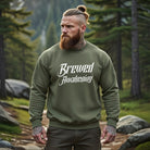 A man with a beard and tattoos wears an olive green crewneck sweatshirt with Brewed Awakening text.